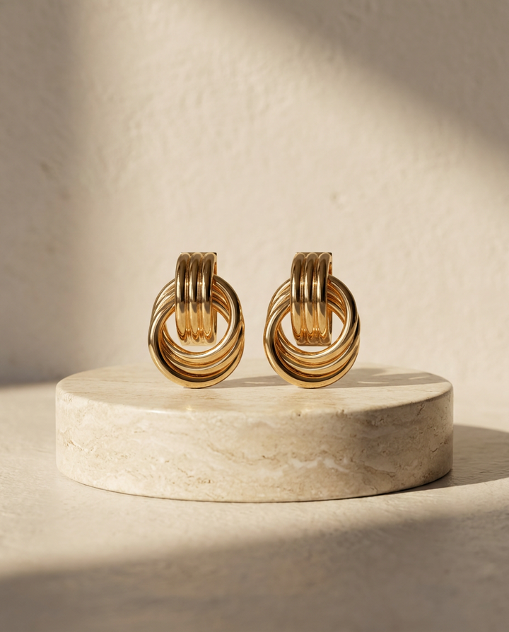 Delphine knotted double hoop earrings on a travertine pedestal in warm afternoon light